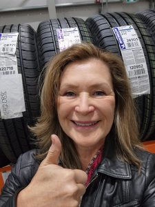 Marion smiling gives a thumbs up in front of a row of Costco tires.