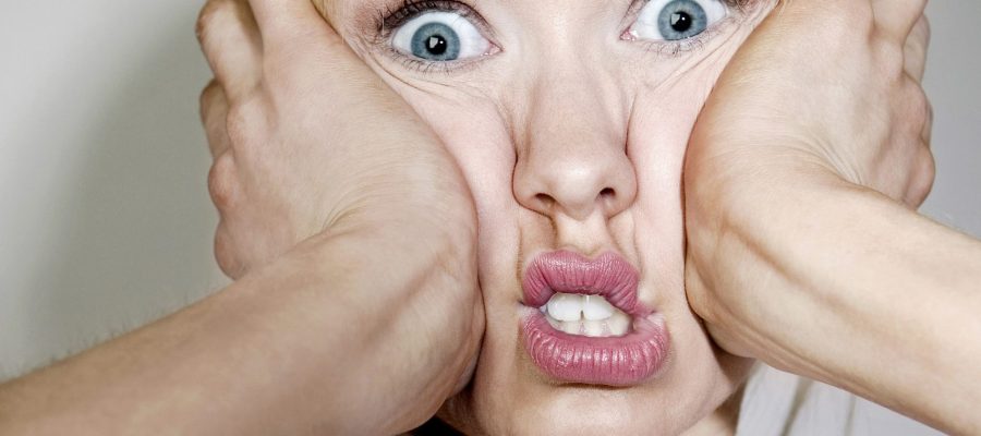 woman looking overwhelmed, wide-eyed and pressing palms to cheeks